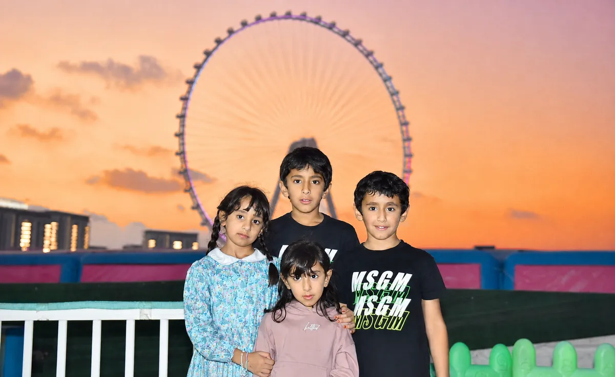 Four children photographed together at sunset with an observation wheel behind them