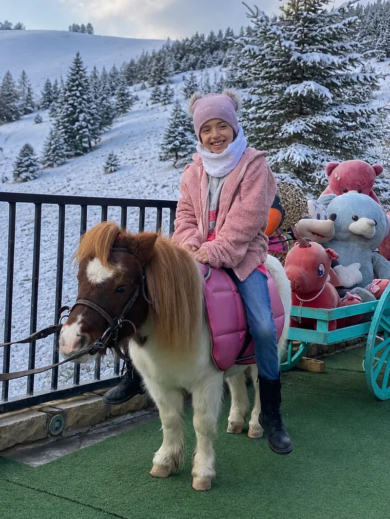 A child in winter clothing sitting on a pony inside an indoor snow park